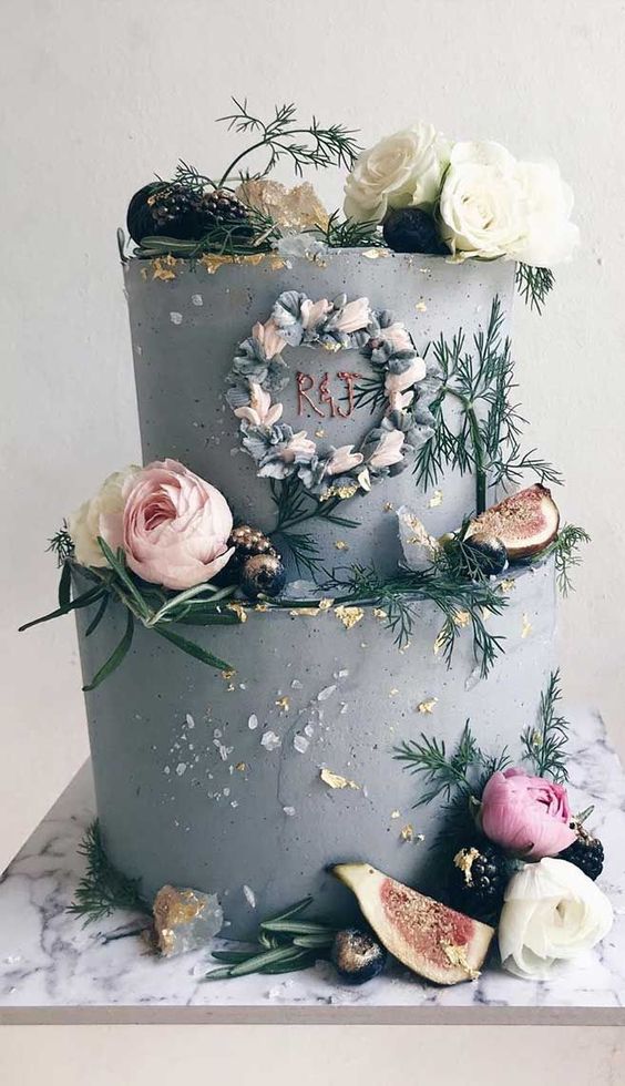 a grey textural wedding cake with fresh blooms, greenery, crystals, gold leaf and fruits plus a copper monogram
