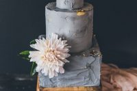a grey textural wedding cake with tiers of different shapes and gold foil, a blush bloom with greenery for a modern wedding