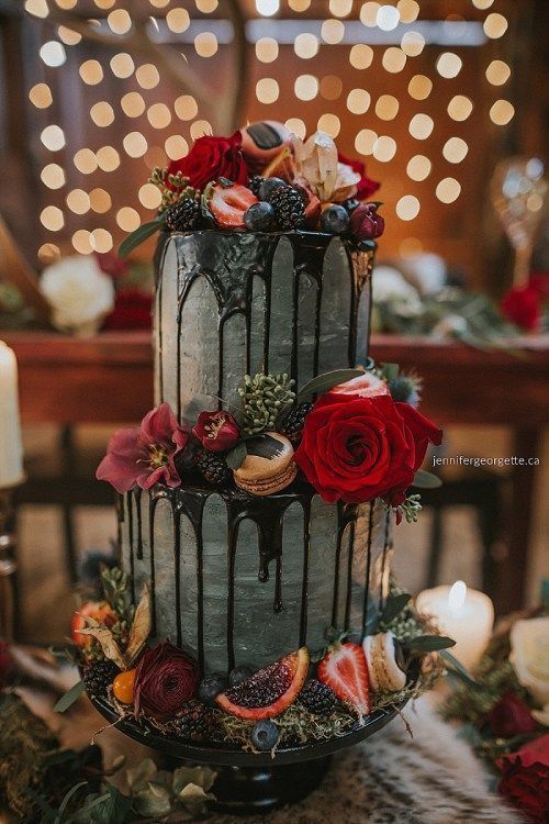 a grey watercolor wedding cake topped with bright blooms, berries and greenery and some macarons plus chocolate drip