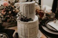 a grey watercolor wedding cake with creamy drip, some white blooms, greenery and berries on it is a lovely idea