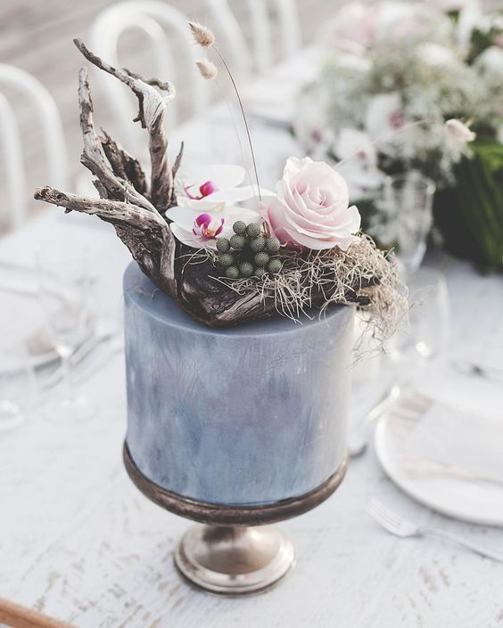 a grey wedding cake with white and pink blooms, driftwood, grasses and berries for a modern coastal wedding