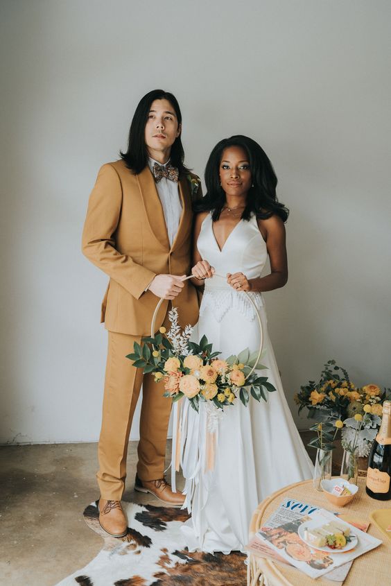 a modern groom's look with a mustard tuxedo, a white shirt, a printed bow tie and brown shoes