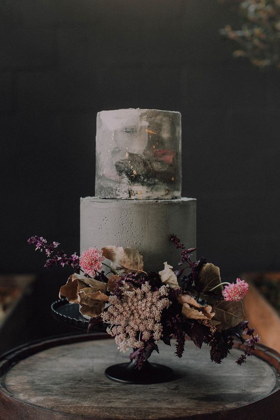 a moody wedding cake with a marble and cocnrete tier, gold touches and bold blooms and leaves for a fall wedding