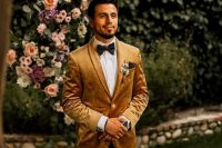 a refined and chic groom’s outfit with a mustard velvet blazer, a white shirt, black trousers, a black bow tie for the fall