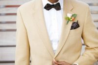 a refined groom’s look with a pale yellow blazer, a white shirt, a black bow tie and black pants, a neutral hat
