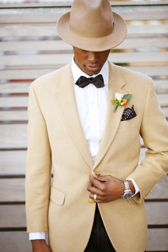 a refined groom's look with a pale yellow blazer, a white shirt, a black bow tie and black pants, a neutral hat