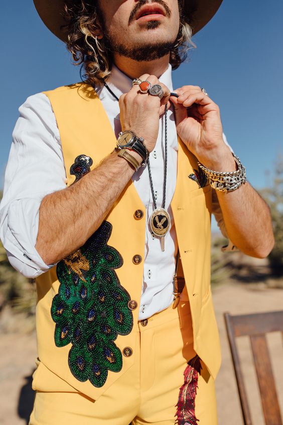 a super bold and badass groom's look with a white shirt, a bold yellow suit with beading, a bolo tie and a cowboy hat