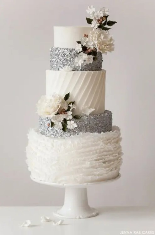 a white and silver wedding cake with silver glitter and patterned tiers and some sugar blooms is a beautiful dessert