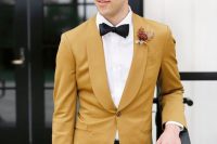 an elegant mustard-colored wedding tuxedo, a white shirt, a black bow tie and black trousers for a chic and color-infused groom’s look