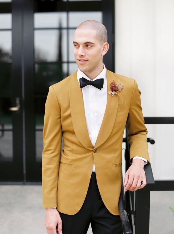 An elegant mustard colored wedding tuxedo, a white shirt, a black bow tie and black trousers for a chic and color infused groom's look