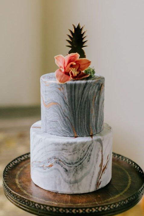 an exquisite wedding cake with grey marble tiers, copper leaf and a bold tropical bloom and a pineapple topper is cool