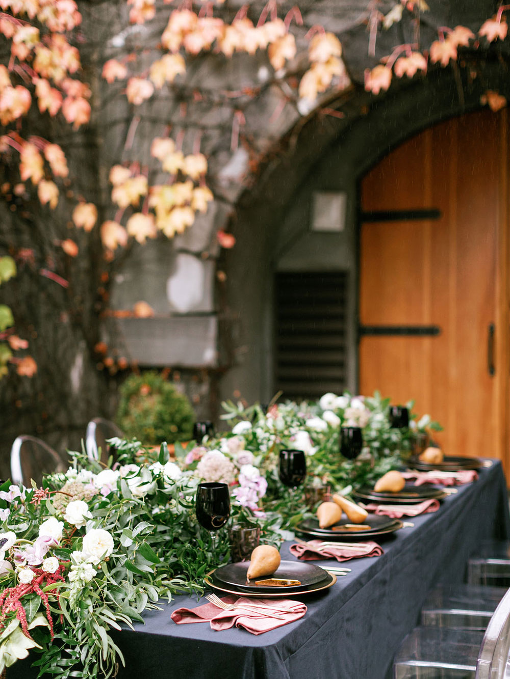 The wedding tablescape was done with a grey tablecloth, pink napkins, black plates and glasses and a lush greenery runner