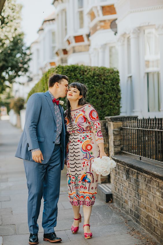 a colorful Mexican-inspired midi wedding dress with a high neckline, long sleeves and bright embroidery, red shoes and a red lip