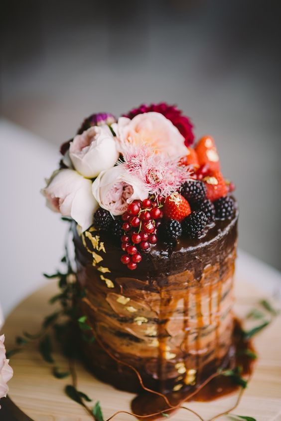 a chocolate wedding cake with drip, fresh berries and blush blooms on top plus gold leaf is a refined and delicious idea