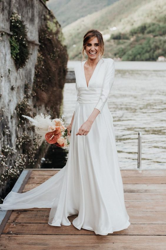 a stunning minimalist A-line wedding dress with a deep neckline, long sleeves, a wide sash and a train
