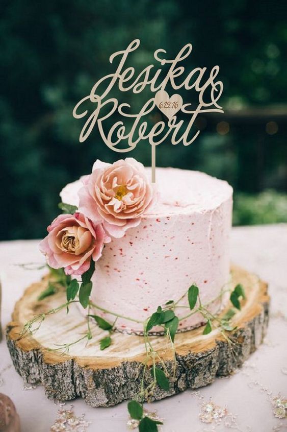 a pink buttercream speckle wedding cake with pink blooms, greenery and a gold calligraphy topper