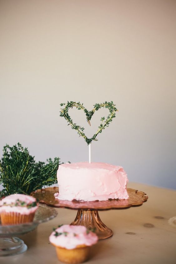 a pink buttercream wedding cake topped with a greenery heart is a simple and very cute idea for an at home wedding