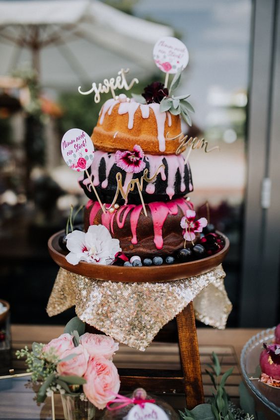 a creative three-tier bundt wedding cake with colorful drip, greenery and bold blooms and funny toppers