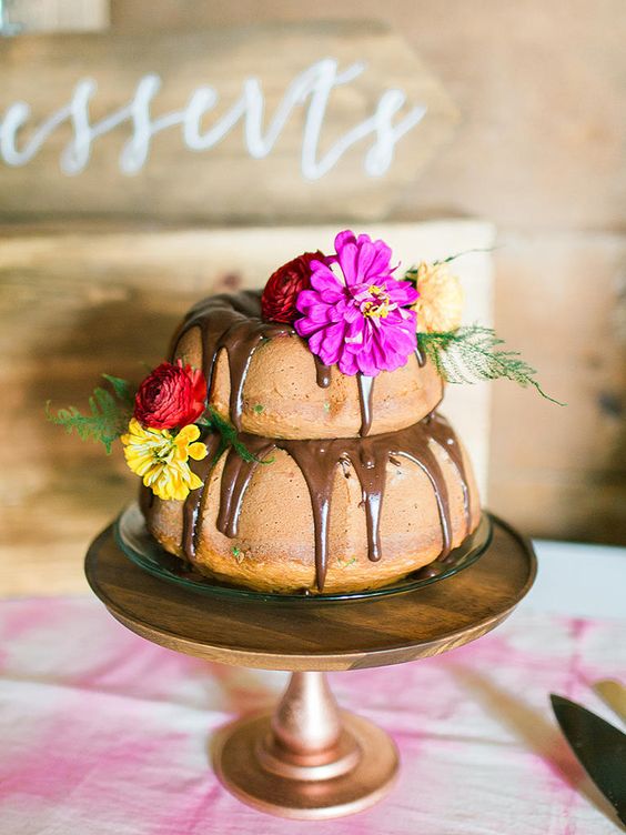 a two tier bundt wedding cake with chocolate drip, bright blooms and greenery is a gorgeous idea for a refined wedding