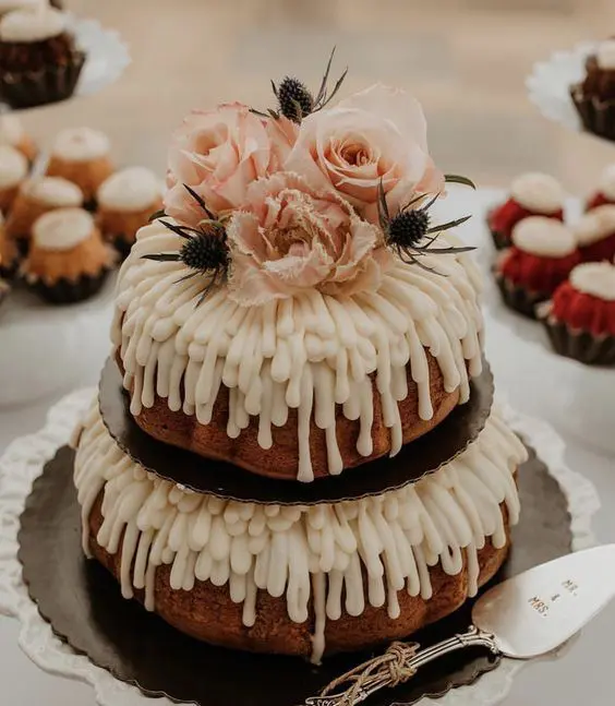 a two tier bundt wedding cake with creamy drip, blush blooms and thistles on top is a stunning idea for spring or summer