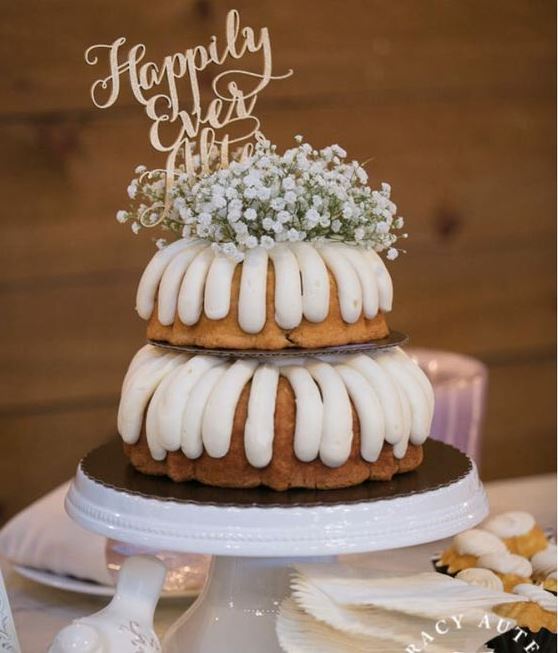 a two-tier bundt wedding cake with frosting, baby's breath on top and a gold calligraphy topper