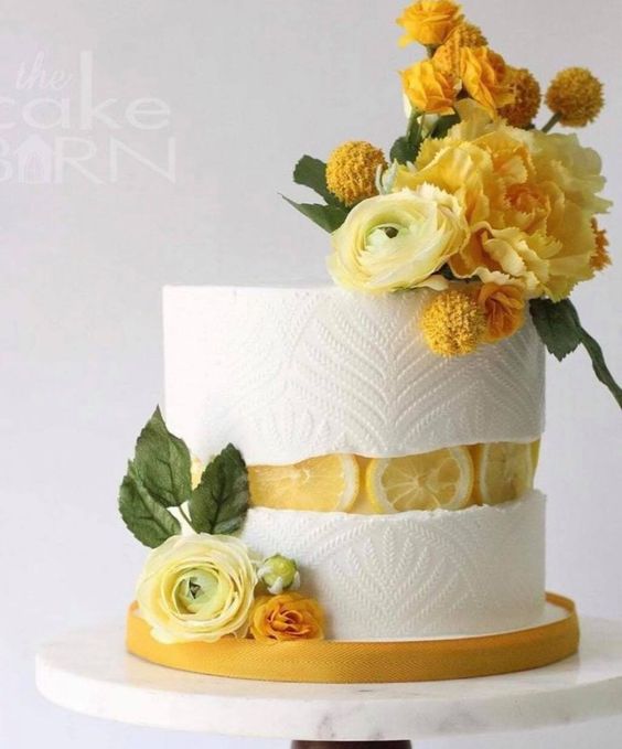 a white patterned wedding cake with a lemon slice fault line and some bold yellow blooms for detailing