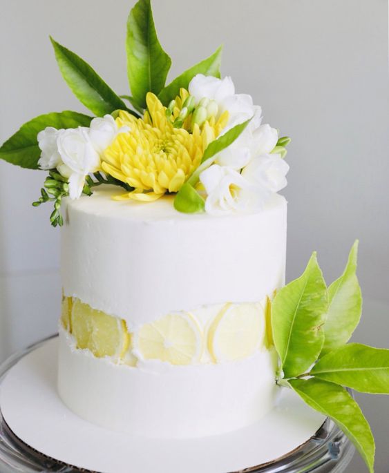 a white wedding cake with a citrus slice fault line, white blooms and yellow ones plus foliage on top
