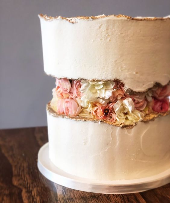 a white wedding cake with a gold edge and fresh blooms in the fault line is a pretty and chic idea for a modern wedding