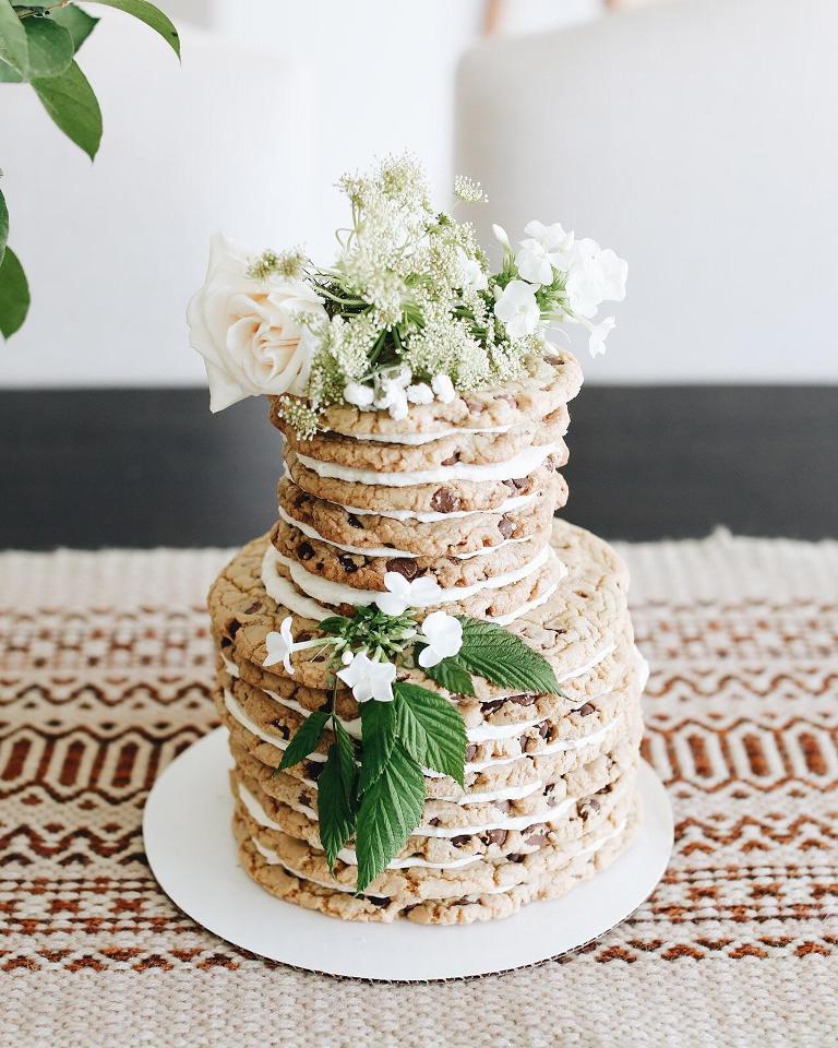 a chocolate chip cookie wedding cake with white blooms, white filling and some foliage looks gorgeous and yummy