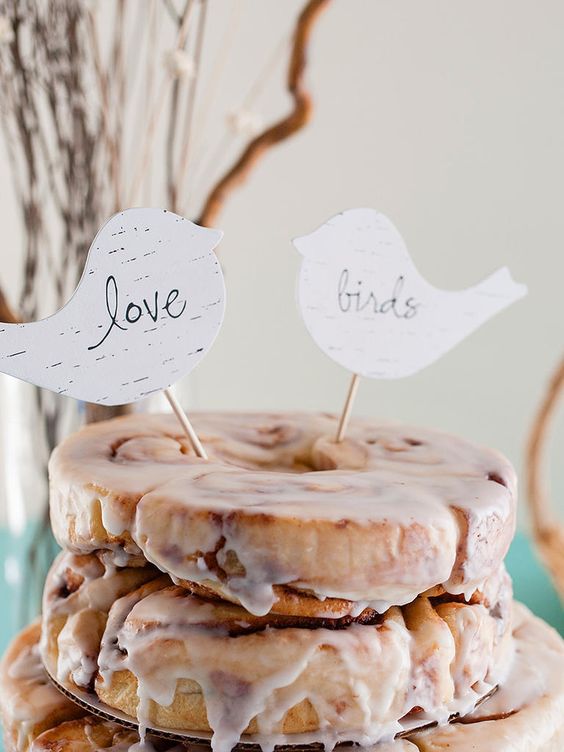 a cinnamon roll wedding cake with multiple tiers, white icing and little plywood toppers shaped as birds