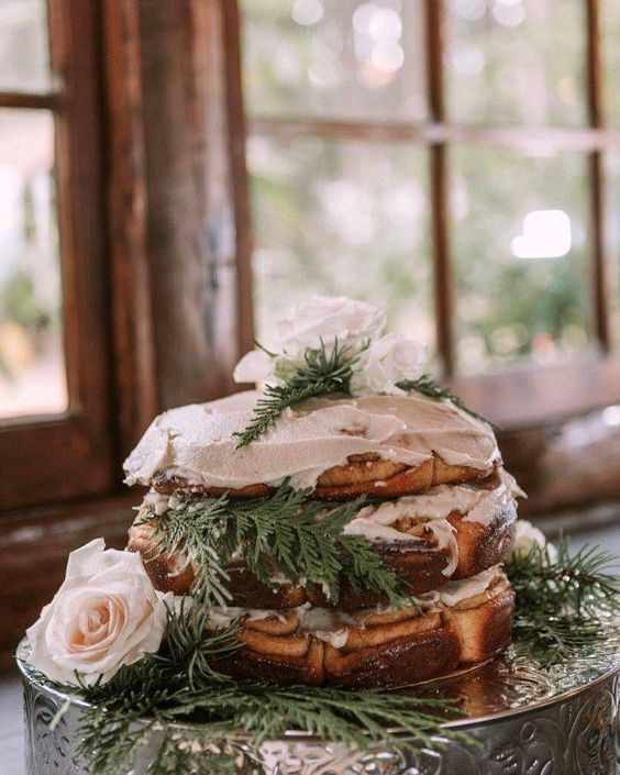 a cinnamon roll wedding cake with white frosting, white and blush blooms and greenery for a laid-back winter wedding