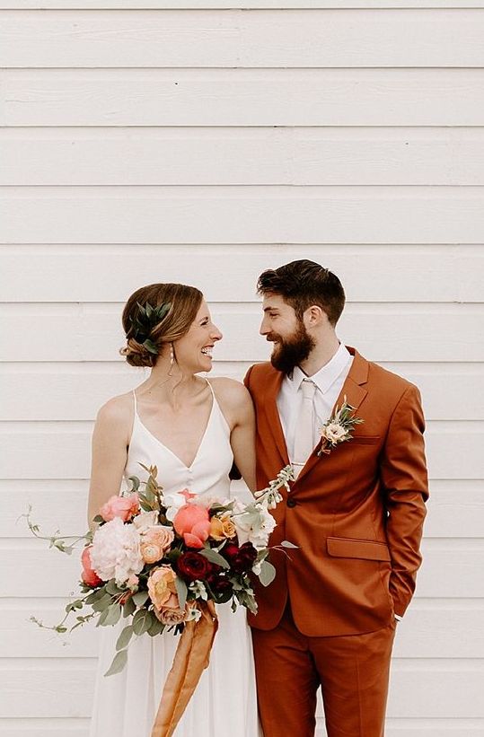a rust-colored suit, a white shirt and a creamy tie, a neutral floral boutonniere for a pretty summer or fall boho wedding