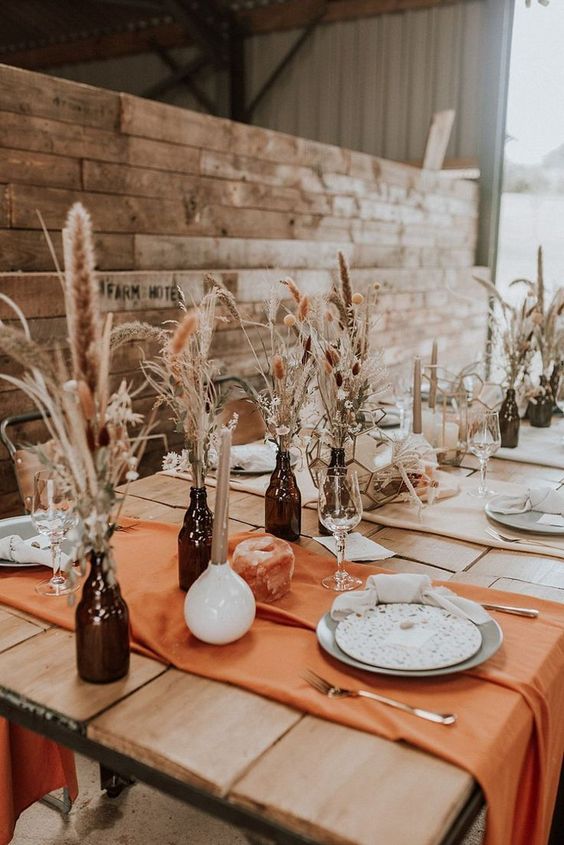 bottles of dark glass and dried grasses plus candles make up chic and cool boho centerpieces