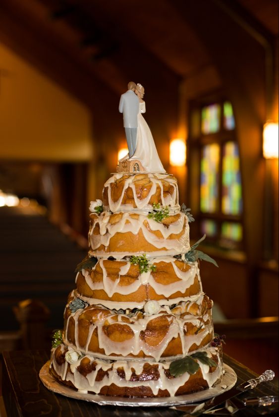 a five-tier cinnamon roll wedding cake with white icing and greenery plus traditional toppers is a very cool idea