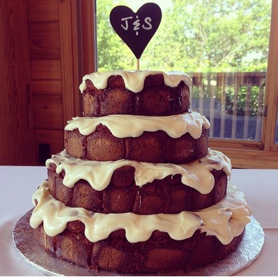 a four-tier cinnamon roll wedding cake with white icing and a heart-shaped chalkboard topper