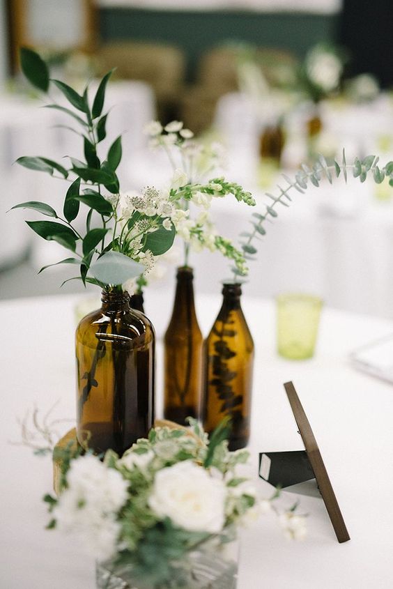 a lovely cluster wedding centerpiece of bottles with greenery and some white blooms is a pretty modern rustic decor idea