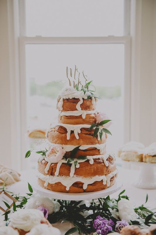 a lovely cinnamon roll wedding cake with white icing, greenery, blush blooms and a calligraphy topper