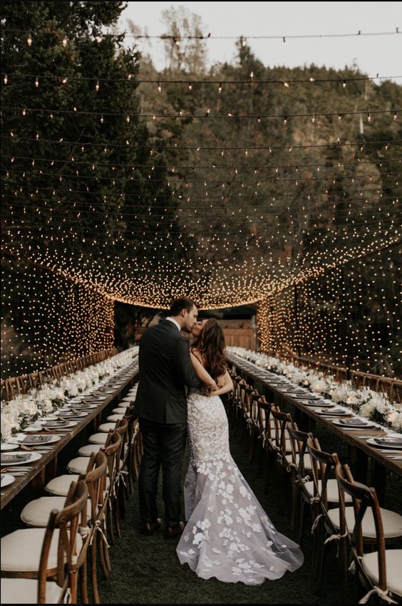 a modern rustic outdoor wedding reception with white blooms and candles and a light canopy over the space is chic