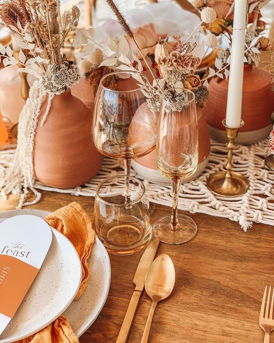 a fall boho wedding table setting with a macrame runner, terracotta vases, dried blooms and grasses and rust napkins