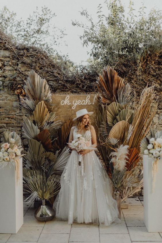a pretty boho wedding backdrop of burlap, a neon sign and colored dried fronds and pampas grass is amazing