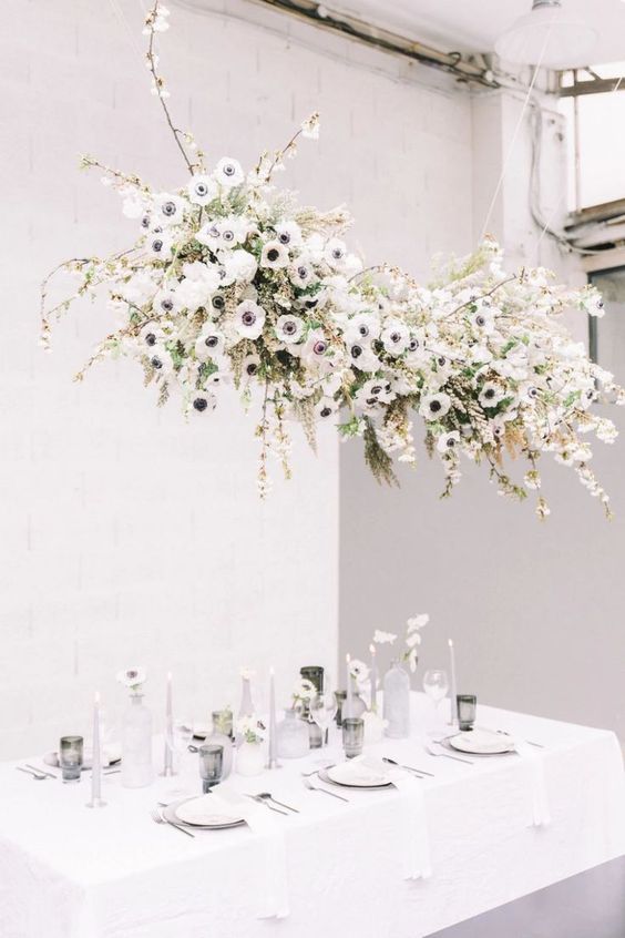 a neutral wedding tablescape with a white anemone hanging over the table, neutral candles and smoked glasses