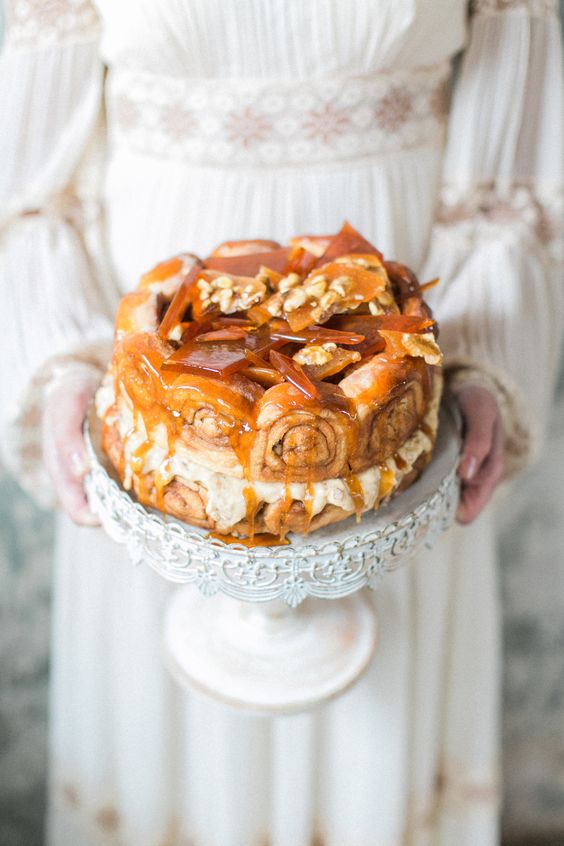 a yummy-looking cinnamon roll wedding cake with white filling, caramel shards and drip on top and some nuts
