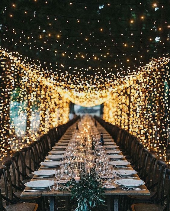 a stylish modern wedding reception with a greenery and candle runner and a light canopy over it is a very chic and beautiful option