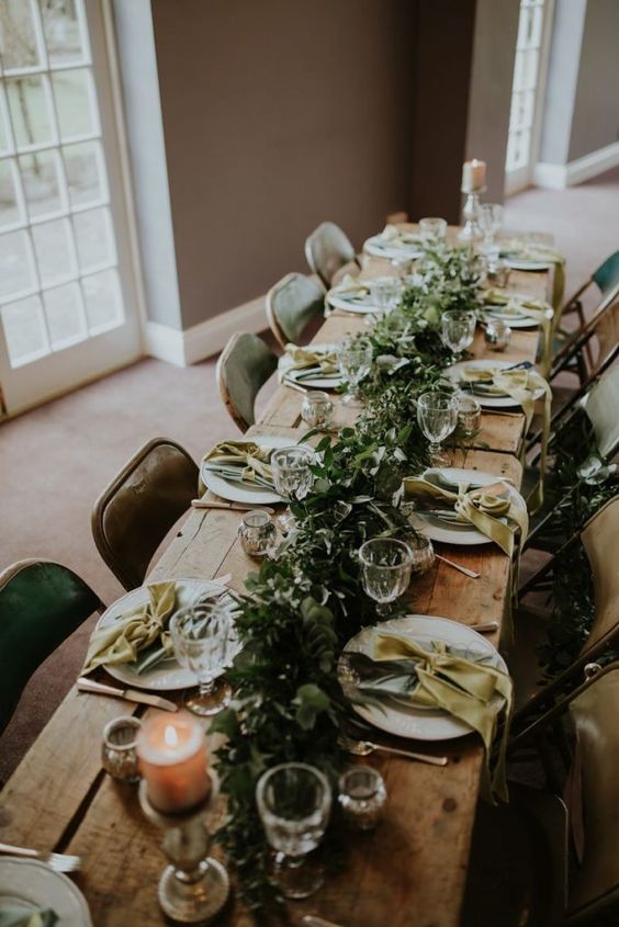 a relaxed summer Scandinavian tablescape with a lush and dimensional greenery runner, candles, bold napkins and neutral porcelain