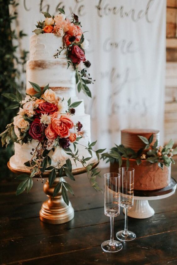 a rust textural wedding cake with berries and foliage plus a naked wedding cake with bright blooms and greenery for a rustic wedding