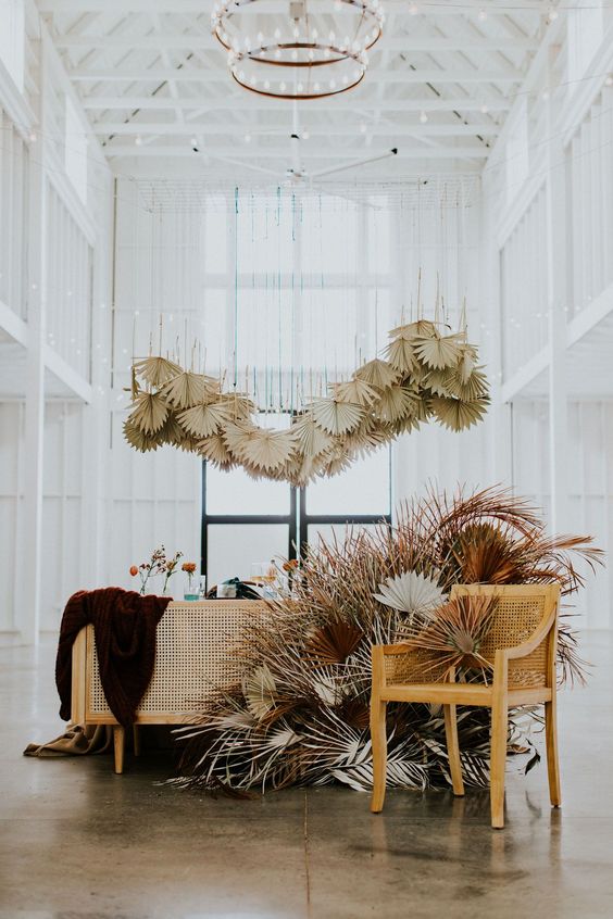 a cool boho wedding reception with a rattan table, dried fronds over the table, fronds in various colors framing the table