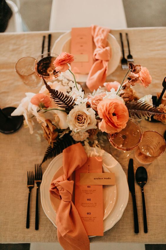 39 a pretty modern wedding tablescape with a rust, blush and orange floral centerpiece, rust napkins and menus, black cutlery