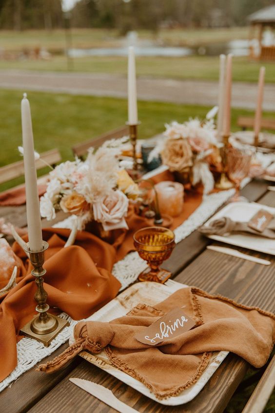 a warm colored wedding tablescape with a rust table runner, antlers, neutral blooms and candles, rust napkins and amber glasses