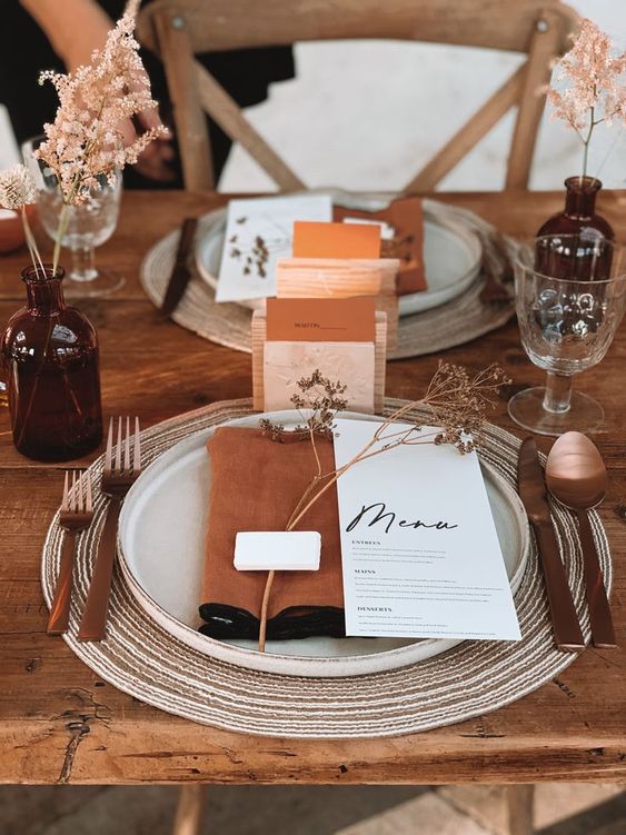 an exquisite wedding tablescape with rust napkins, menus and blooms, amber bottles and white porcelain