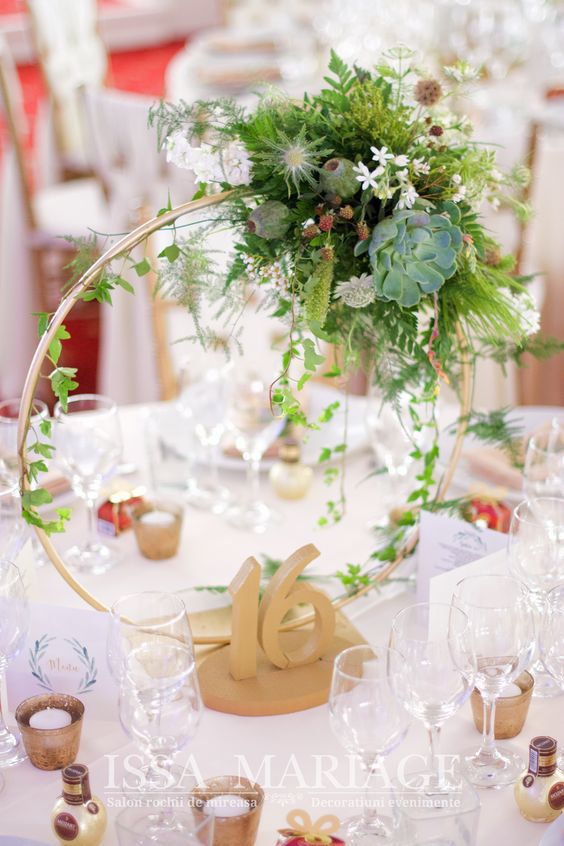 a stylish hoop wedding centerpiece with greenery, succulents and some white blooms and a wooden table number